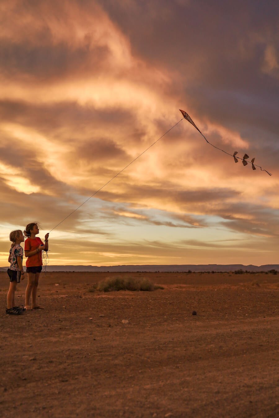 Kids flying a kite in Morocco at sunset.