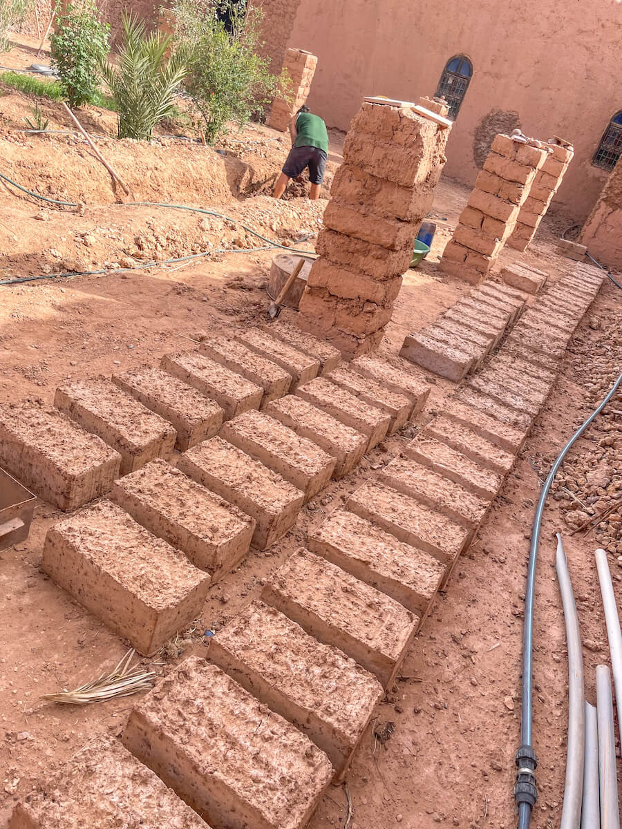 Mud bricks lied out to dry, with a man working in the back ground preparing more.