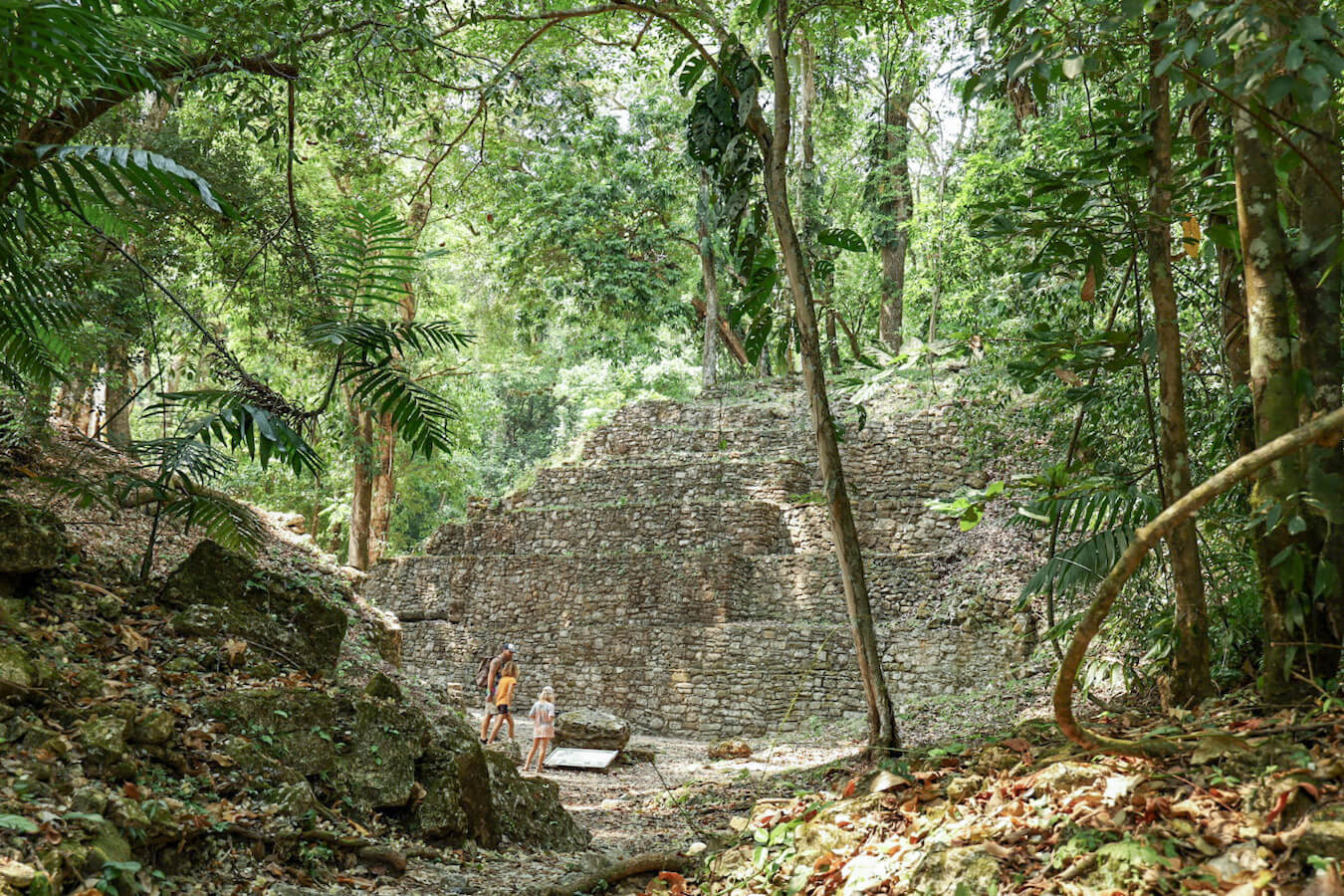A father and his two daughters exploring a section of the Yaxchilán ruins, surrounded by jungle. 
