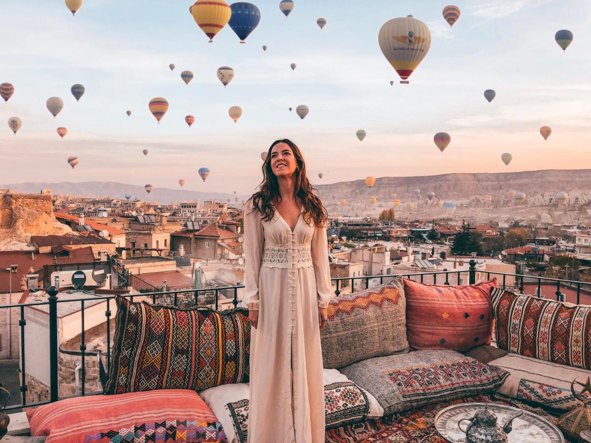 A woman stands one of the best cave hotel terraces in Cappadocia and admires hot air balloons flying in the distance.